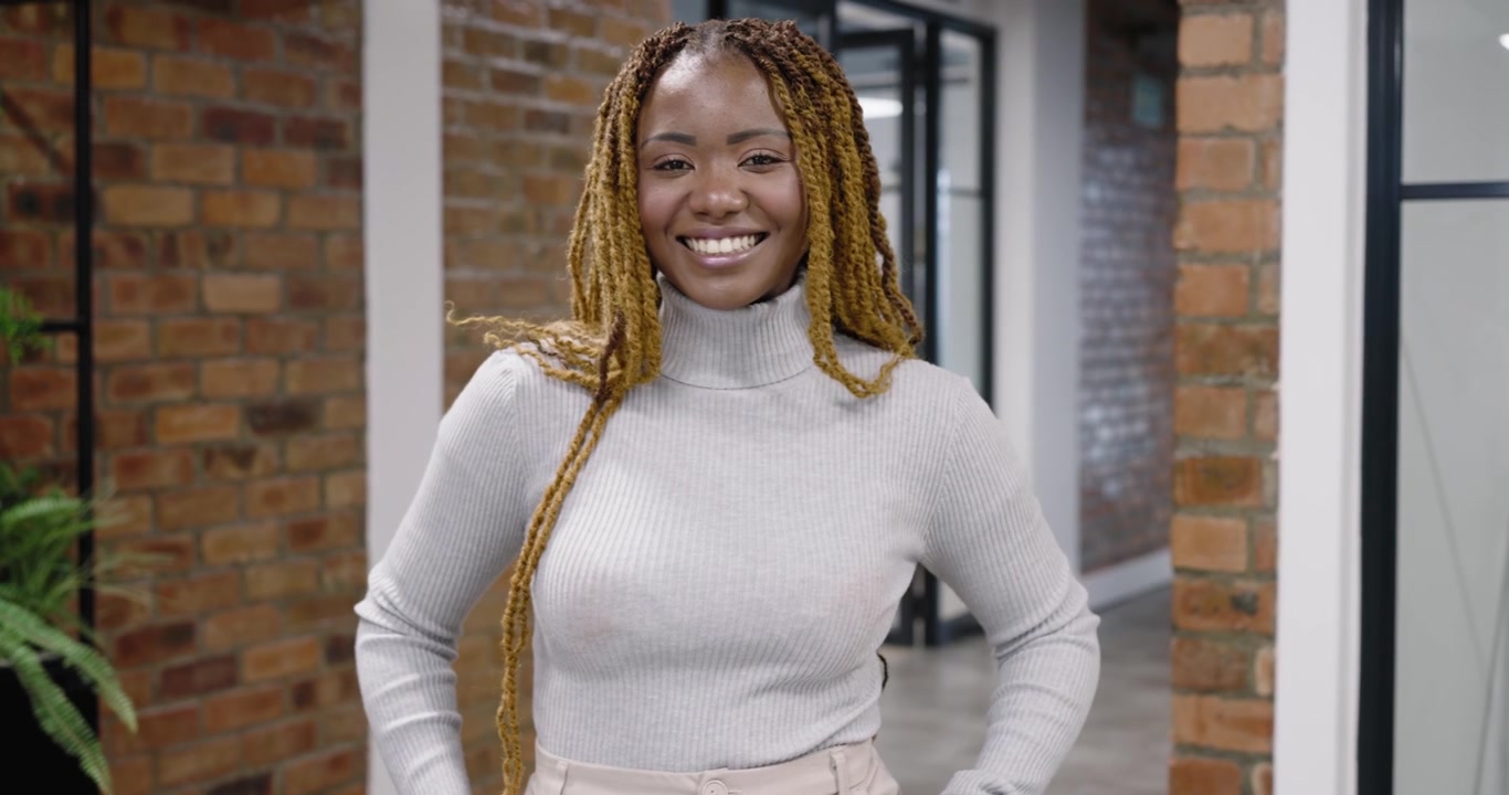 Midaldrende afrikansk kvinde iført sweater på kontor, kamera nærmer sig, tjekker armbåndsur for tid.