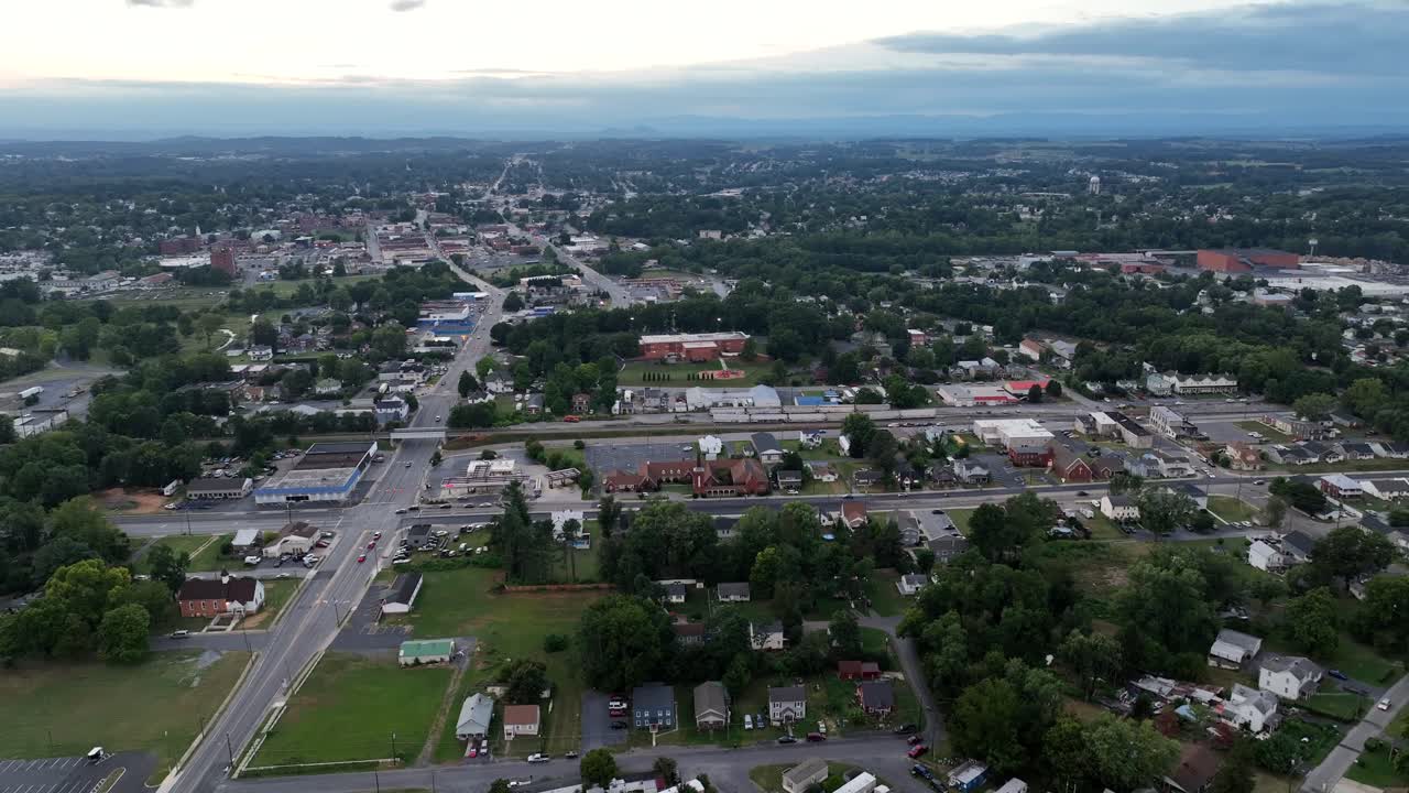 Mobile trailer homes and traffic on Main Street in American town. Aerial rising wide shot. Grey clouds at sky in Virginia state. Dark evening dusk. Suburbia with downtown in background