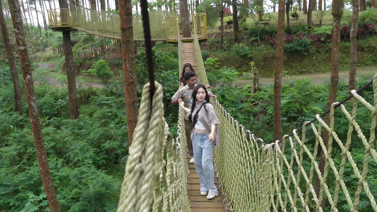 Young Asian Friends Crossing Rope Bridge in Forest Adventure