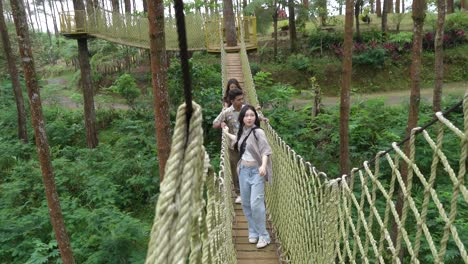 young asian friends crossing rope bridge in forest adventure