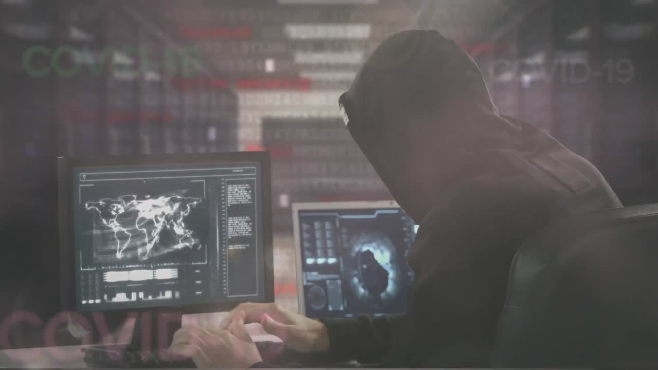 Animação de palavras COVID-19 sobre um homem encapuzado hacker em dois computadores em uma sala de dados