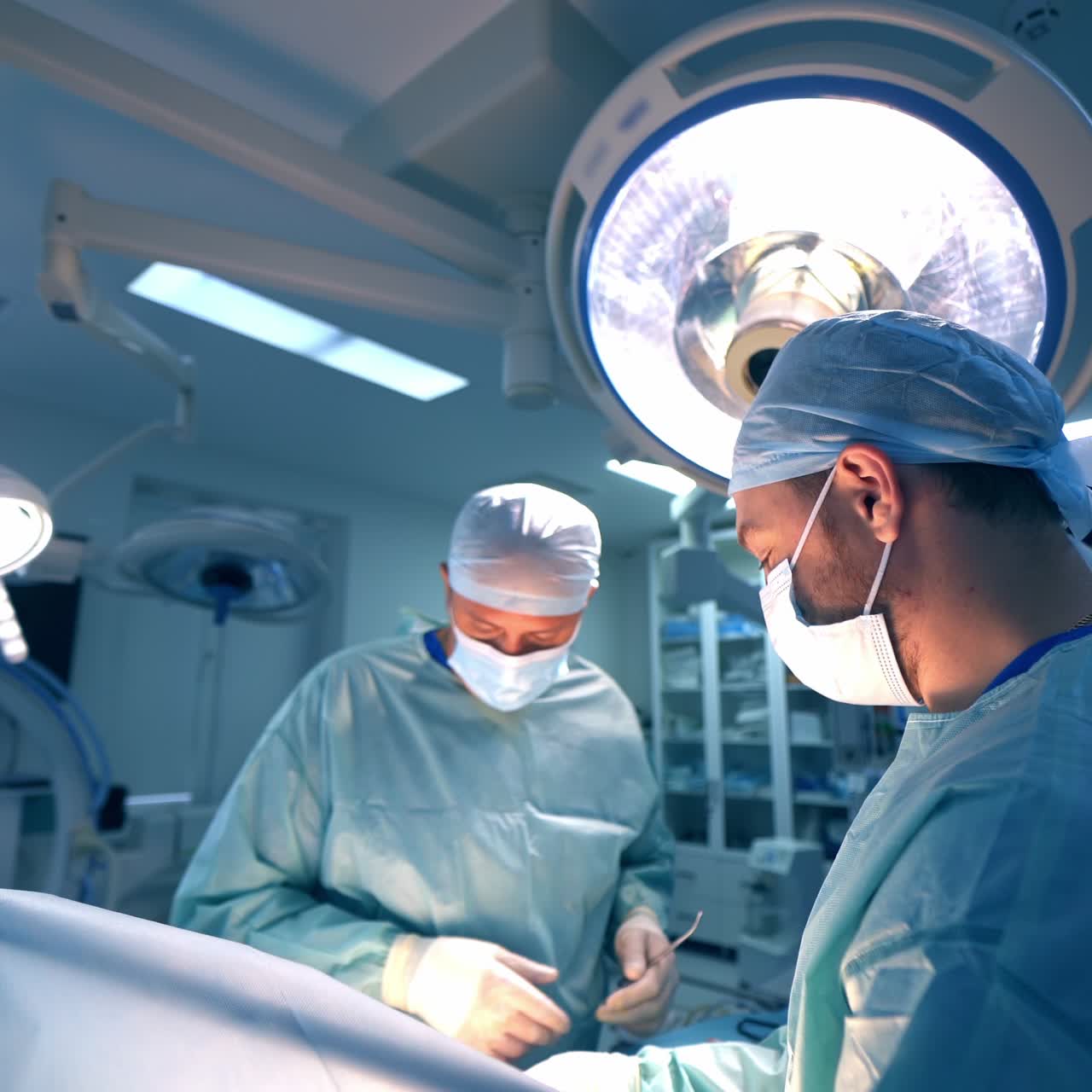 Confident Caucasian surgeon acts actively during operation. Doctor changes instruments quickly while performing operation. Equipped modern operation room backdrop