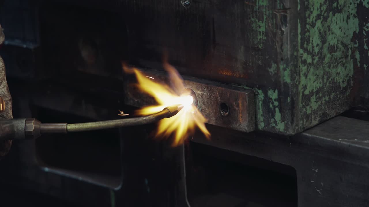 Close-up of a worker welding machinery in an industrial workshop with a soldering iron producing intense flames