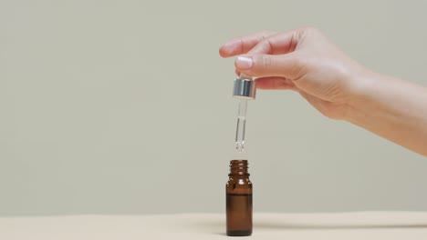 Hand-of-woman-taking-cosmetic-from-flask-on-grey-background-with-copy-space,-slow-motion