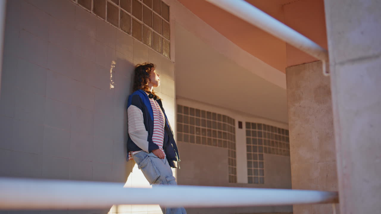 ティーンエイジャーの女の子がガムバブルを吹く 都市の建物に寄りかかっている リラックスした女性がリラックスしている