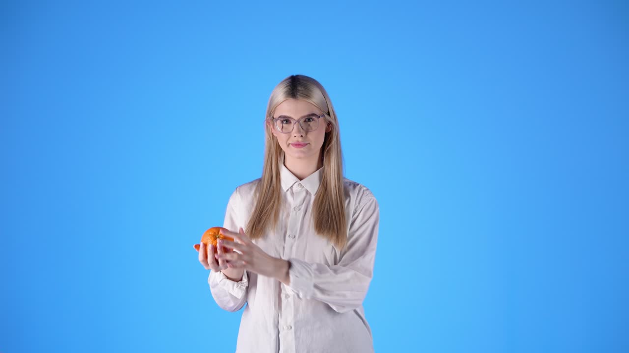 mujer feliz lanza una naranja, malabarismo de frutas, toma de estudio, fondo azul