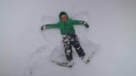 young boy making snow angels while snow gently falls, slow motion