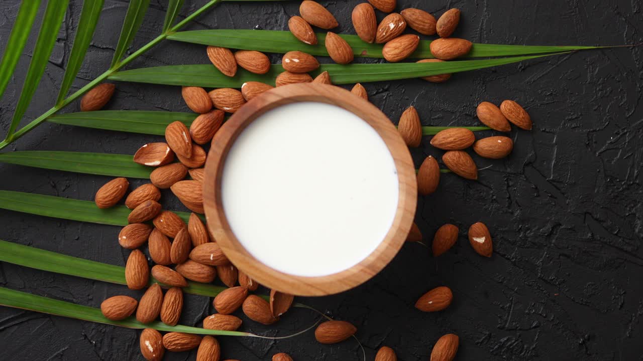 semillas de almendras con tazón de leche natural fresca colocada sobre fondo de piedra negra