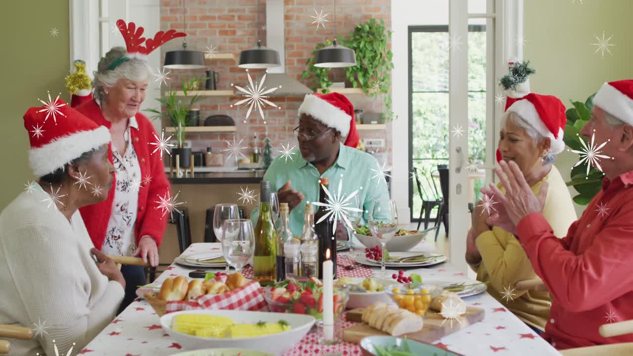 animación de la nieve cayendo sobre los viejos amigos diversos en sombreros de santa en la mesa de la comida de navidad.