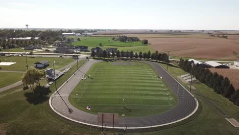 aerial drone footage of high school football field and tall brown fields ready for harvest in rural, midwest iowa corn country