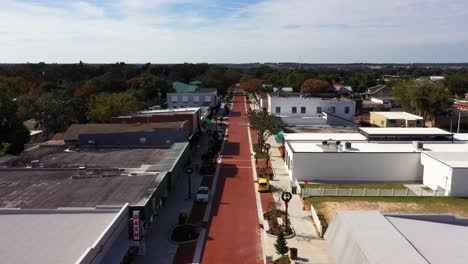 Aerial-dolly-along-red-brick-main-street-road-lined-with-shops-at-midday