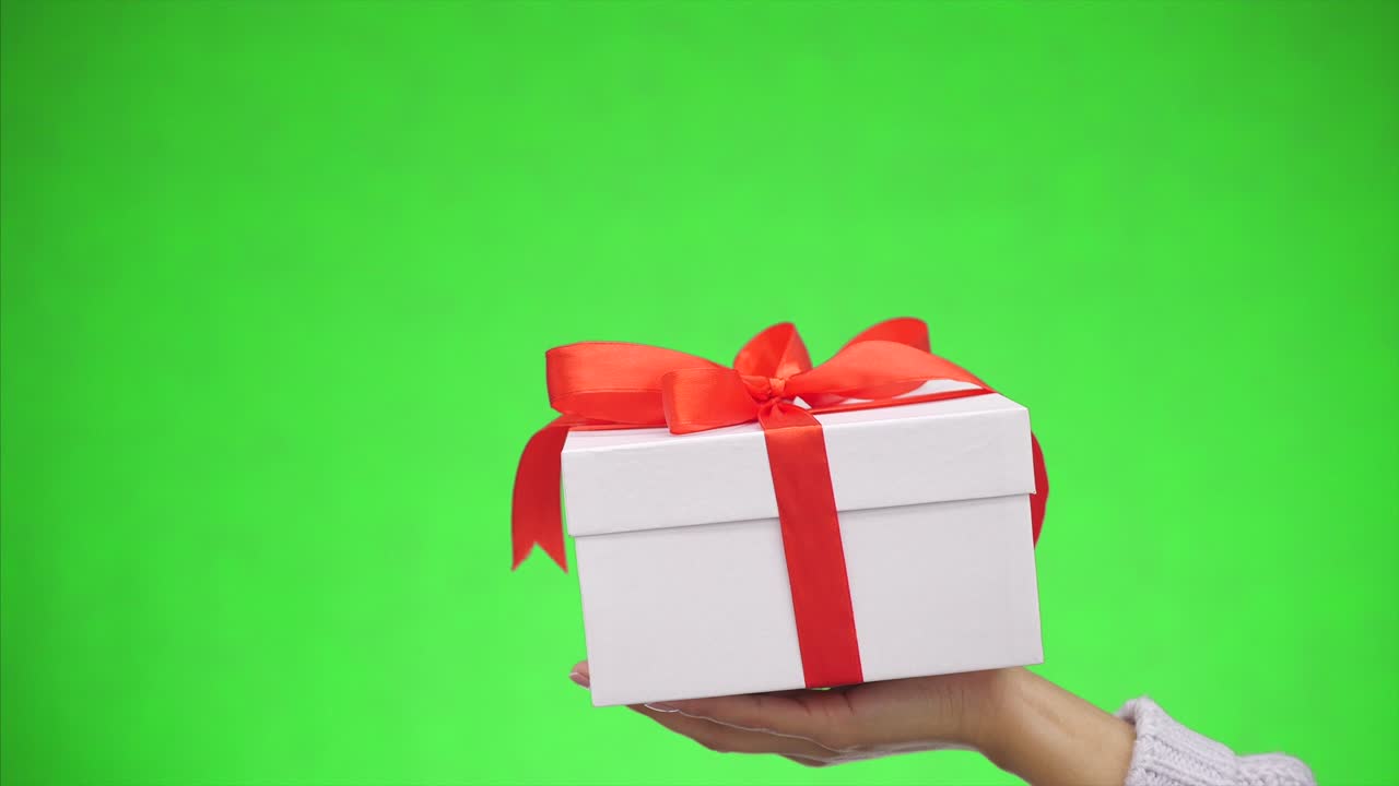 la caja de regalos blanca atada con un arco de cinta roja está aislada sobre un fondo verde. mejores deseos. cerca. espacio de copia.