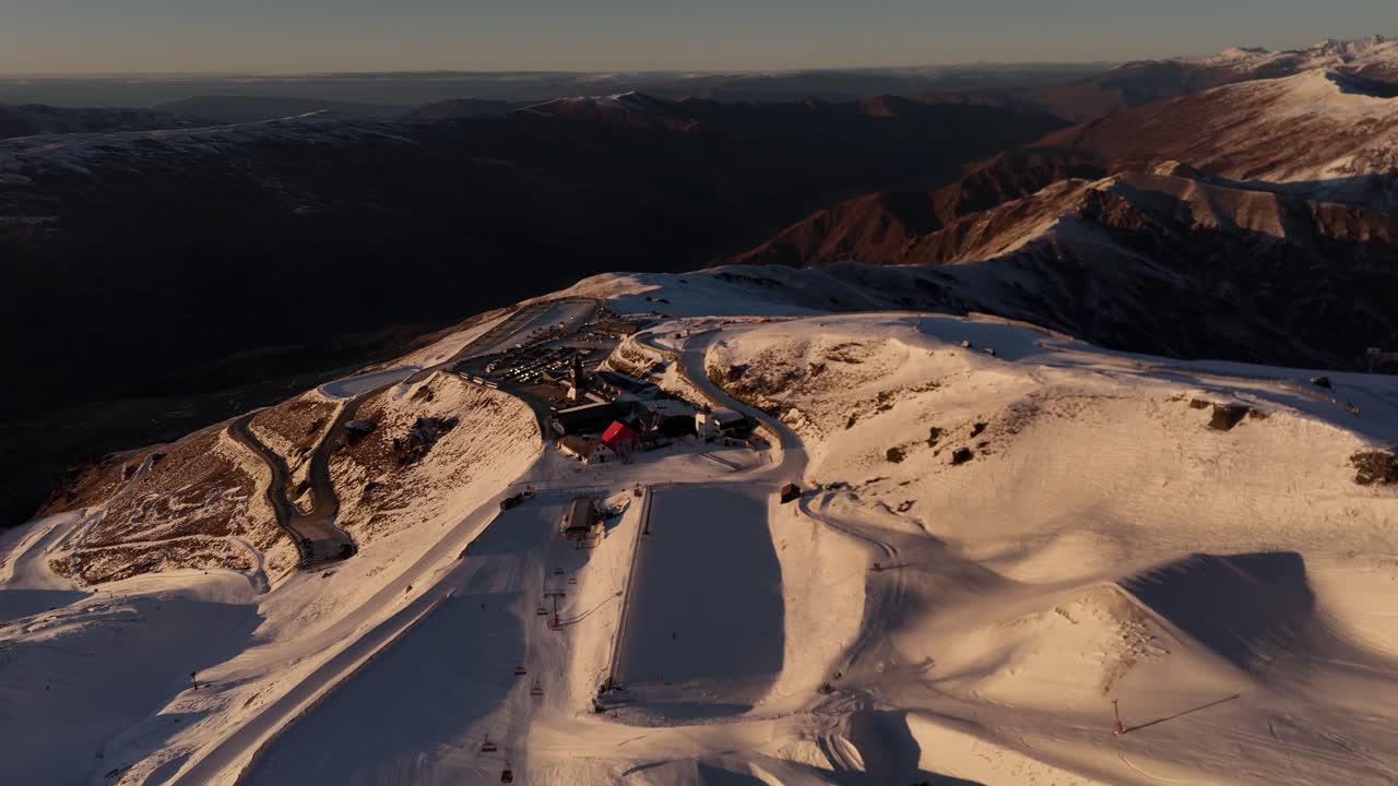 Rotating aerial view of Cardrona Ski Resort in New Zealand at golden hour revealing the snow-covered mountain top and ski slopes