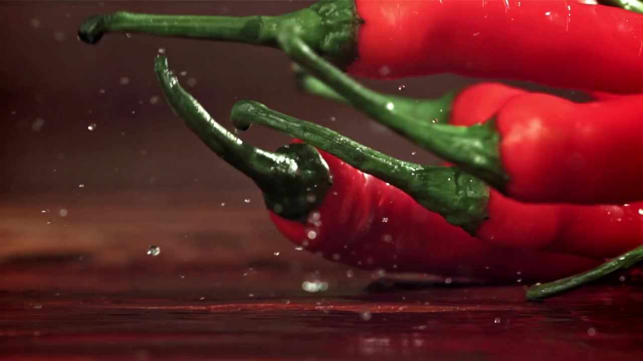 Zářivě červené chilli papričky padající s cákanci vody ve zpomaleném záběru