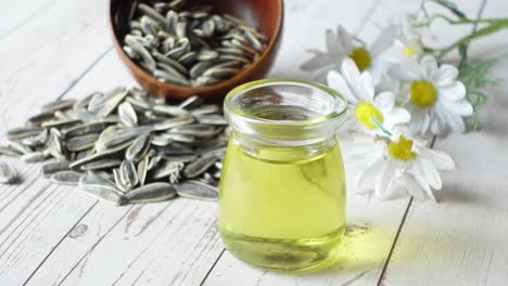 sunflower oil, seeds and daisies on a white wooden table