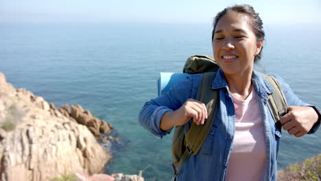 hiking on mountain trail, woman with backpack smiling near ocean cliffs