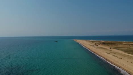 Ascending-revealing-aerial-drone-shot-of-a-peninsula-that-extends-into-the-ocean-over-a-golden-sandy-shore-and-the-blue-sea-of-Mediterranean-sea-close-to-Thessaloniki,-Greece-in-Epanomi