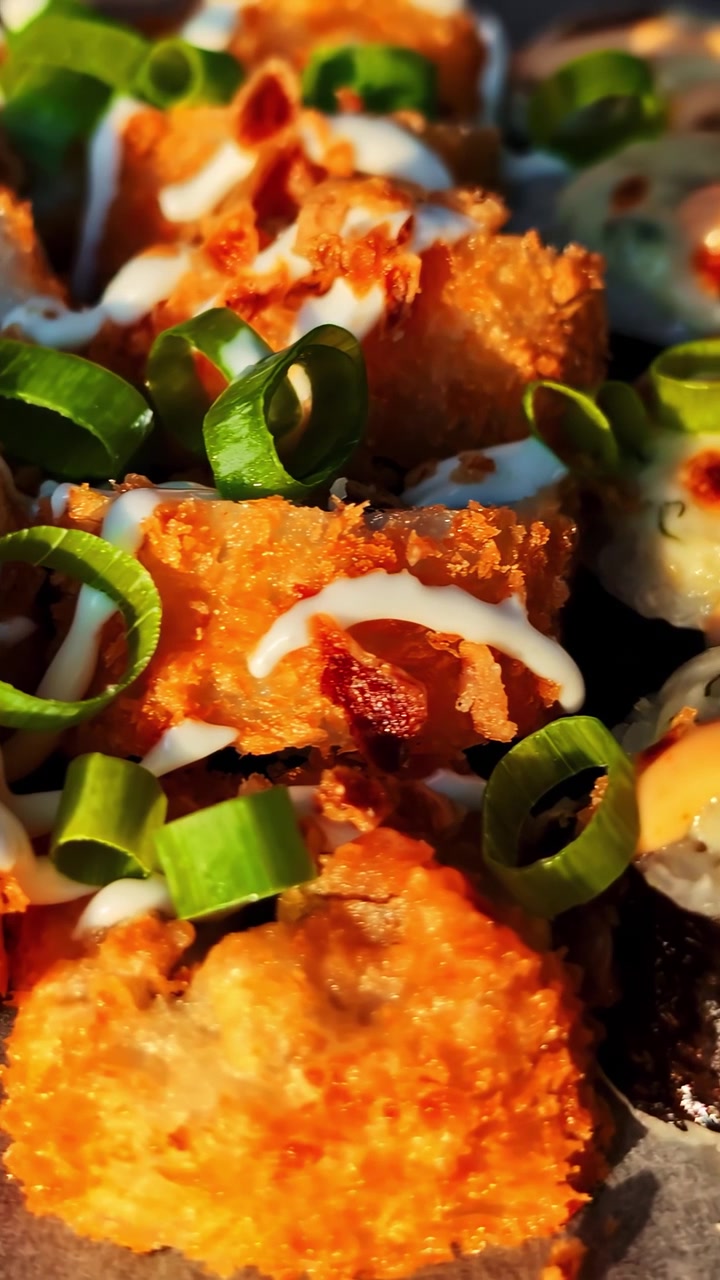 Primo piano di involtini di sushi al forno conditi con maionese piccante e guarniti con cipollotti freschi. Perfetto per blog di cucina o programmi di cucina che mostrano la cucina fusion.