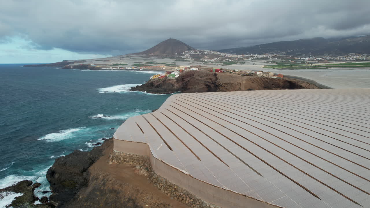 maravillosa toma aérea en punta de galdar sobre invernaderos y al fondo la montaña de galdar y las casas construidas en la costa