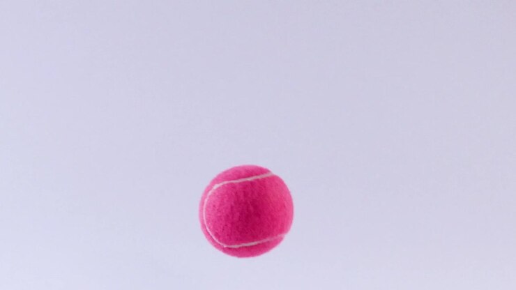 A pink tennis ball appears suspended in mid-air against a clear, light background.