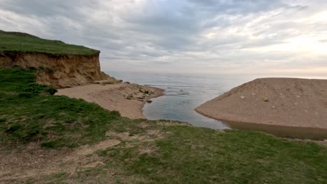 video moving forward towards an ocean inlet river on a jurassic south coast beach. this stabilised footage starts on grass then moves forward to reveal the river cutting through the sand on cloudy day