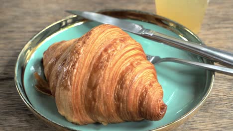 Panning-from-right-tp-the-left-on-a-plate-with-one-serving-of-croissant,-served-on-a-plate-with-a-glass-of-fruit-juice