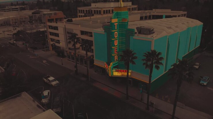 Vista aerea cinematografica dall'alto del centro di Roseville, California, con edifici industriali, negozi e il teatro a torre accanto a un parcheggio multipiano durante il tramonto e auto di passaggio