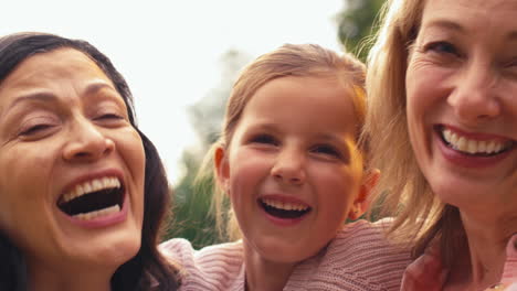 Close-Up-Portrait-Of-Same-Sex-Family-With-Two-Mature-Mums-Hugging-Daughter-On-Walk-In-Countryside