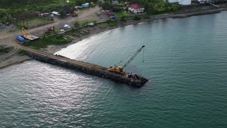 visión aérea en órbita de la grúa amarilla en lo alto de un sitio de construcción de rompeolas rodeado de aguas oceánicas turquesas durante el día