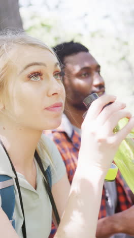 vertical video of happy diverse couple drinking water in park, slow motion