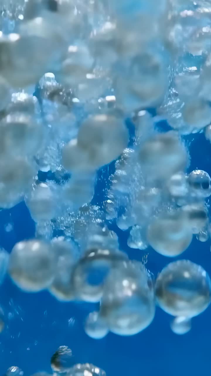 Video verticale: rilascio di una nuvola di bolle che si rompe in sfere trasparenti e sale in un serbatoio blu con riflessi