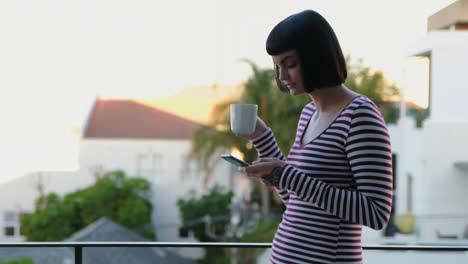 Woman-having-coffee-while-using-mobile-phone-in-the-balcony-4k