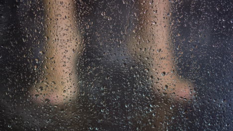 Woman-washes-feet-behind-shower-booth-with-drops-of-water