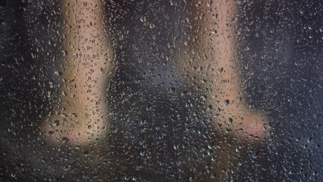 mulher lava os pés atrás da cabine do chuveiro com gotas de água