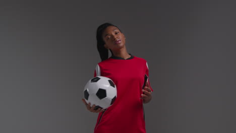 Studio-Portrait-Of-Serious-Female-Football-Or-Soccer-Player-Wearing-Team-Shirt-Holding-Ball-Under-Her-Arm-Shot-Against-Grey-Background-2