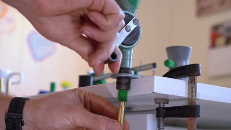 manos usando una medida de polvo para llenar una carcasa de rifle de latón brillante con la cantidad exacta exacta de pólvora - proceso de recarga de municiones en el hogar