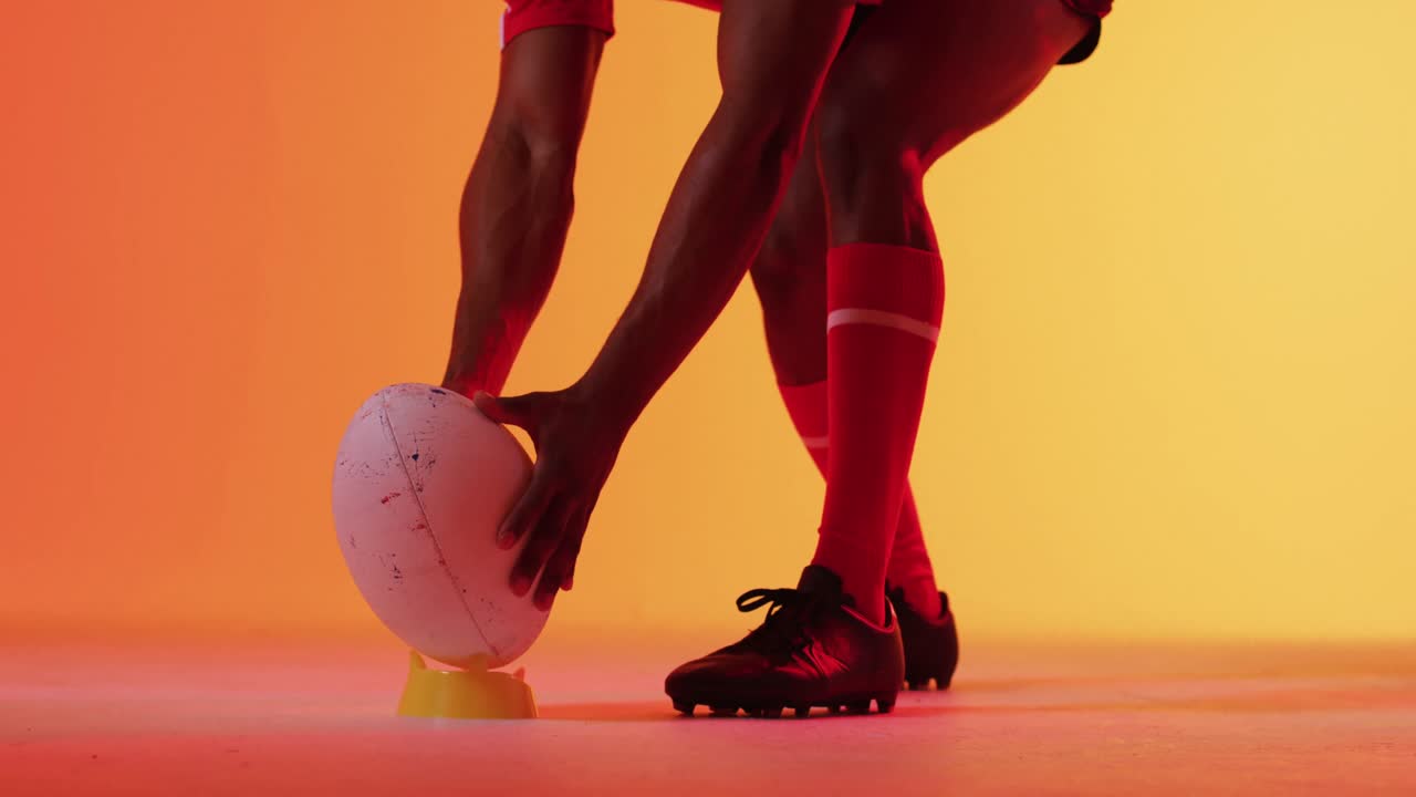jugador de rugby afroamericano acurrucado con una pelota de rugby sobre una iluminación naranja