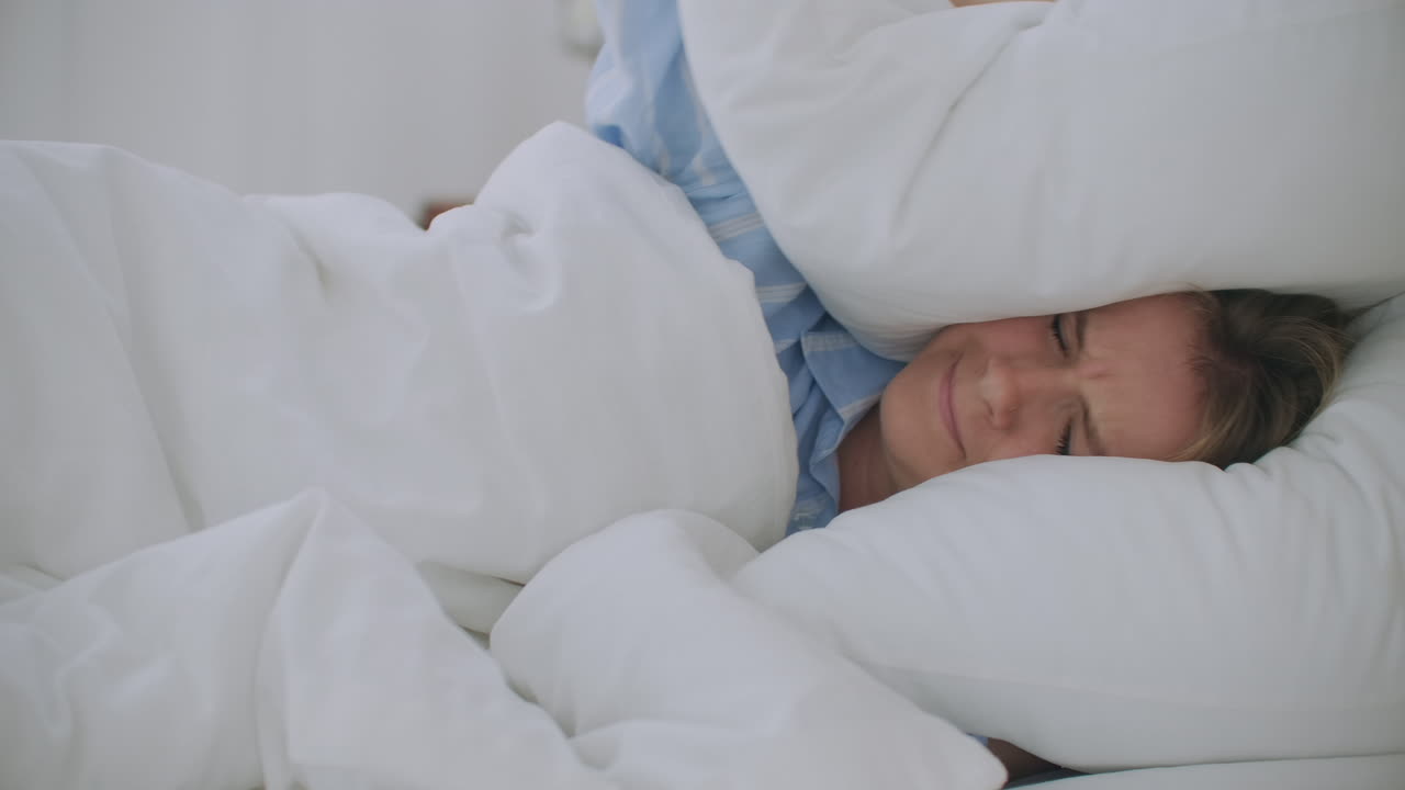 mujer joven irritada tratando de dormir molesta por la mala habitación ruidosa vecinos cubriendo las orejas con almohada chica estudiante enojada perturbada por el ruido fuerte problema despertarse acostado en la cama sufren de insomnio