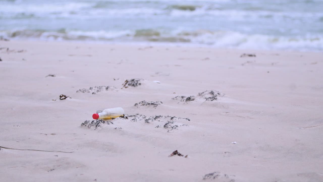 pequeña botella de vidrio en la playa, basura y desechos en una playa vacía de arena blanca del mar báltico, problema de contaminación ambiental, día nublado, plano medio