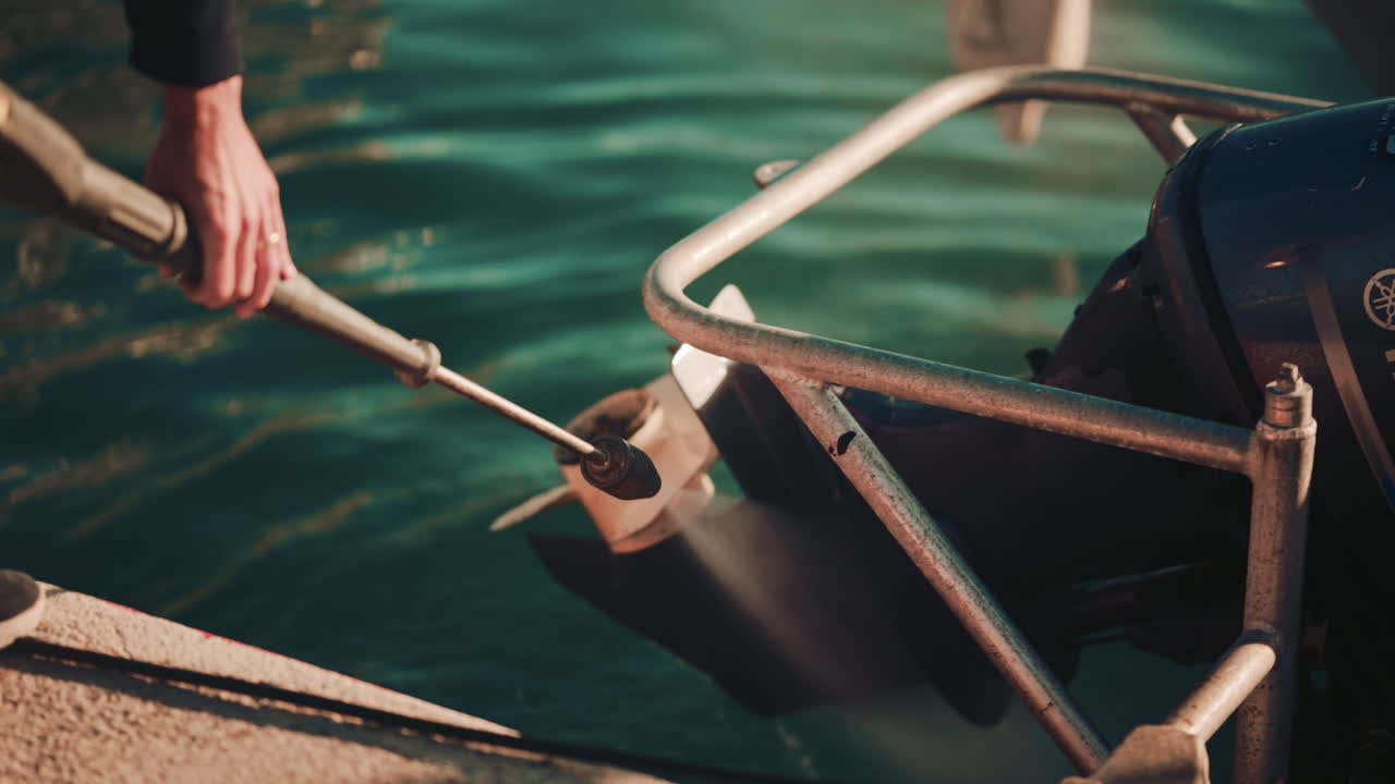 Close up of a man using a pressure washer to clean a boat propeller at the edge of a marina
