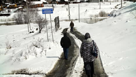 personas caminando por un camino nevado cerca de un río en un pueblo
