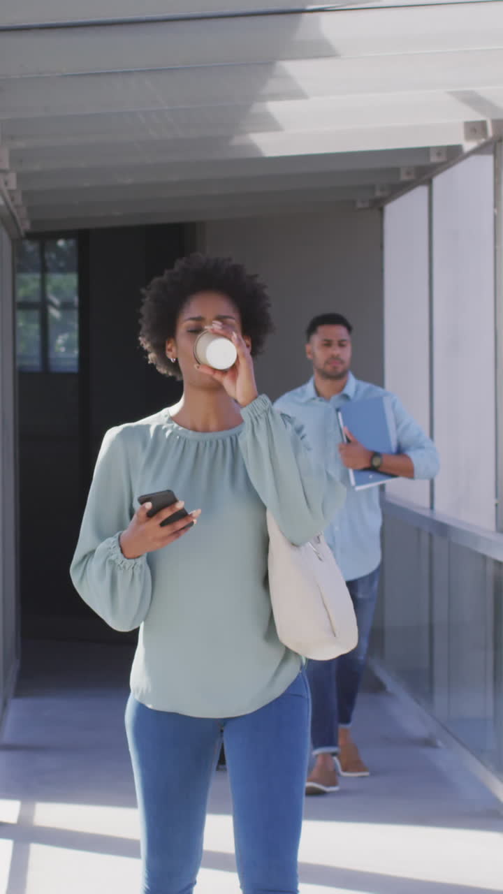 Video of african american businesswoman walking with smartphone and coffee in office