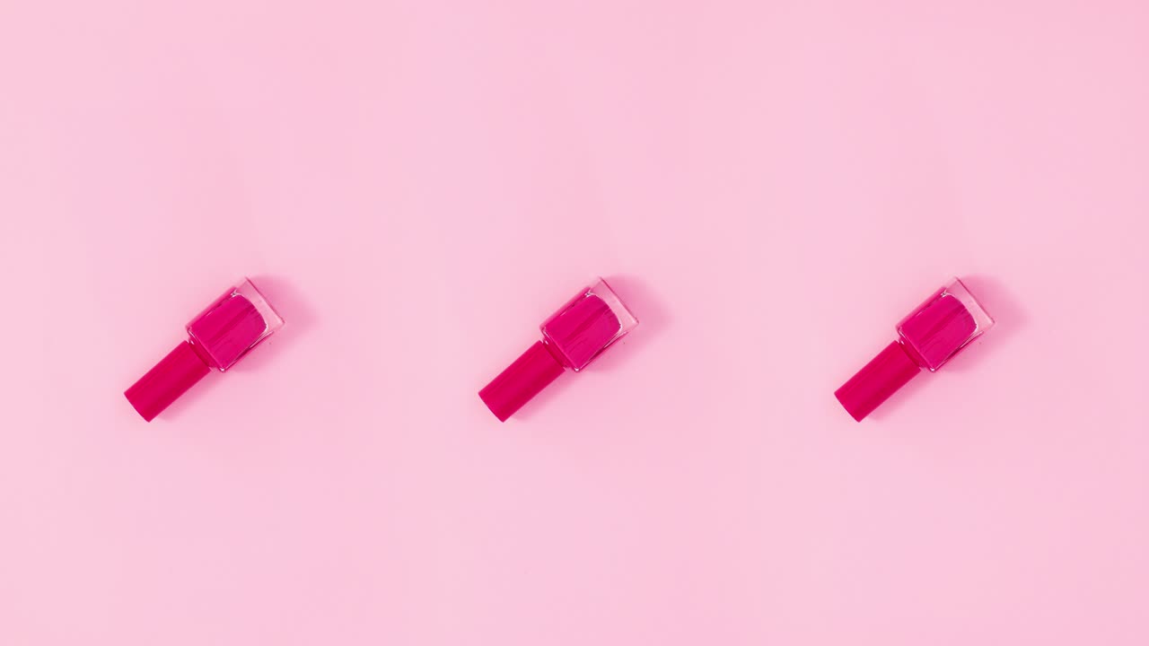 tres botellas de esmalte de uñas giran sobre un fondo rosa pastel. detenga el movimiento