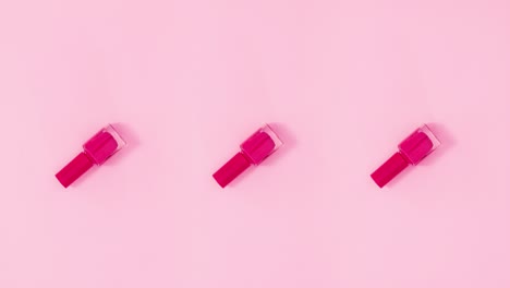 tres botellas de esmalte de uñas giran sobre un fondo rosa pastel. detenga el movimiento