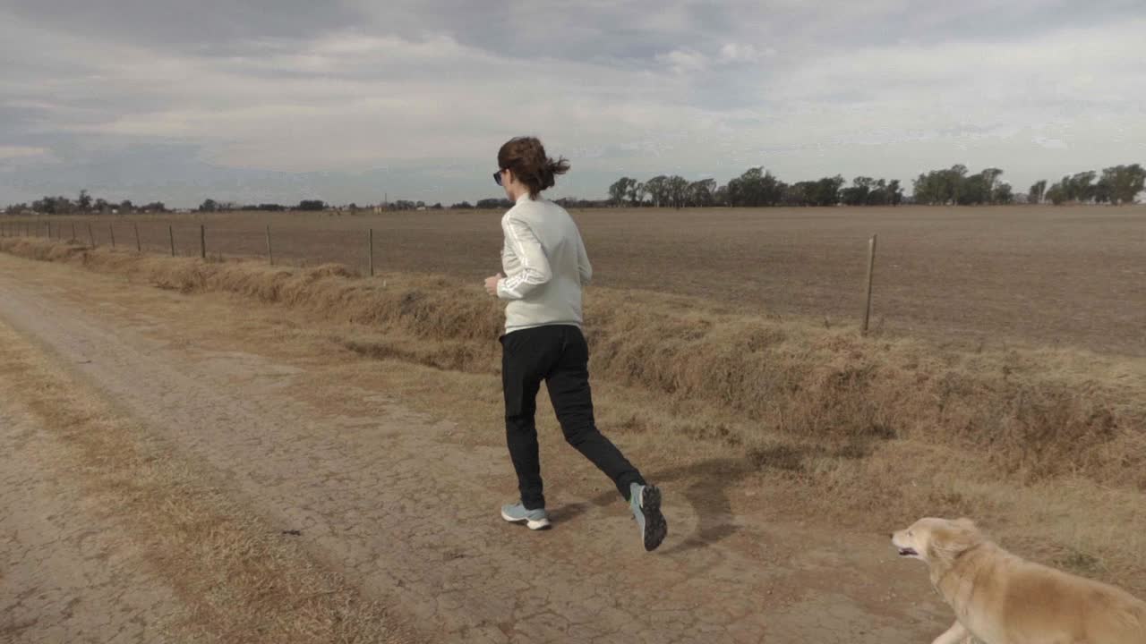 Rallentatore, ampia veduta di una giovane donna adulta che corre con il suo cane domestico su una strada rurale.