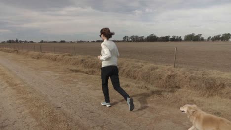 slow motion, wide view of a young adult female running with her pet dog in a rural road