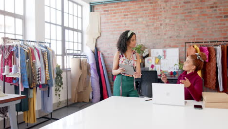 Diverse-female-fashion-designers-using-tablet-and-laptop-talking-at-studio,-copy-space,-slow-motion