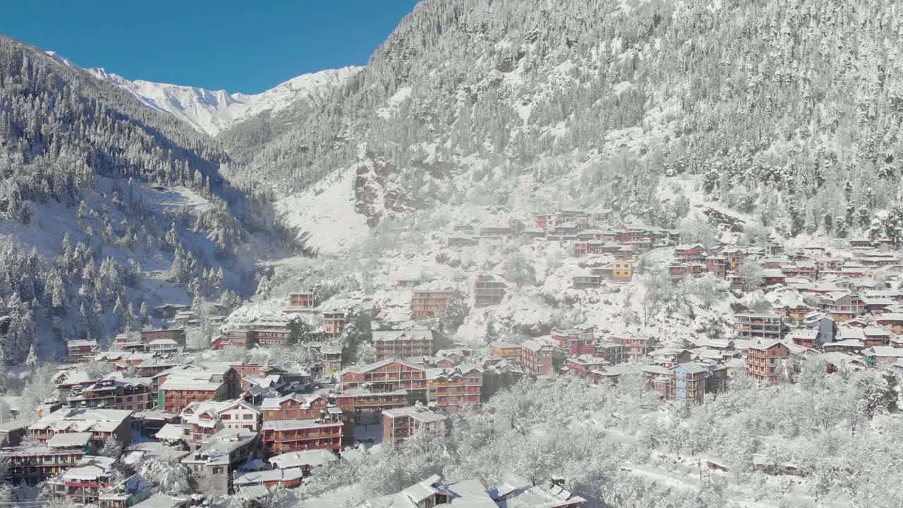 Aerial Zoom-Out Dolly shot of Sunlight hitting Old-Manali town in the morning covered with white snowflakes after receiving a heavy snowfall during the winters of 2020, shot with a drone in 4k