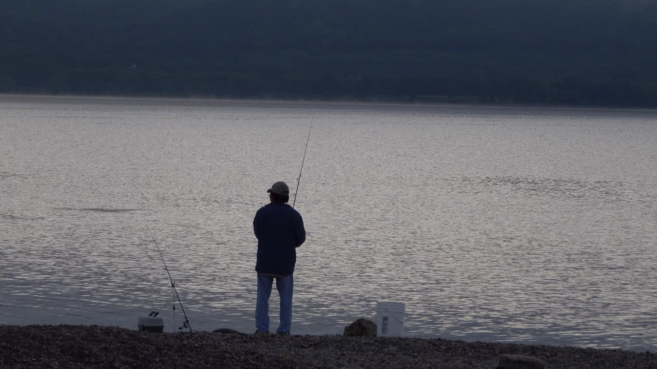 Seorang Pria Memancing di Tepi Danau yang Tenang Saat Fajar