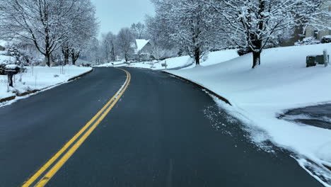 driver point of view in snowy winter scene with neighborhood homes and houses after snowstorm covers trees